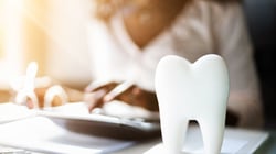 Dental office staff reviewing finances with a model tooth on the desk, symbolizing dental billing and revenue management.