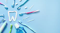 Assorted toothbrushes, dental floss picks, toothpaste, and mouthwash arranged in a flat lay on a bright blue surface.