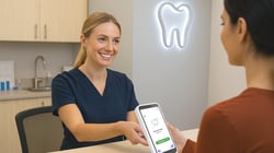 Dental patient using a card terminal for dental payment processing at the front desk, while a smiling dental team member assists in a modern dental office.