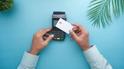 Hands holding a credit card over a payment terminal, representing digital payment processing systems used in dental practices.
