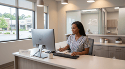 Dental office administrator reviewing practice performance data on a monitor at the front desk, warm lighting, modern clinic background.