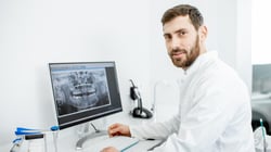 Dentist reviewing a panoramic dental X-ray on a computer monitor in a modern dental office.