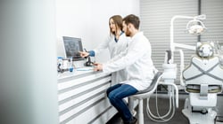 Two dentists sitting at desk, looking at x-ray software on a desktop computer