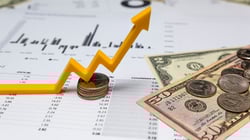 Coins, dollar bills, and an upward arrow on financial charts, representing growth in dental practice revenue