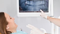 Patient smiling looking at X-Ray while dentist points at imaging screen. 