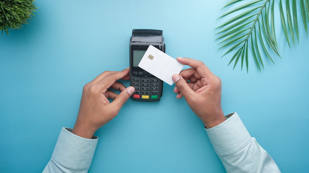 Hands holding a credit card over a payment terminal, representing digital payment processing systems used in dental practices.