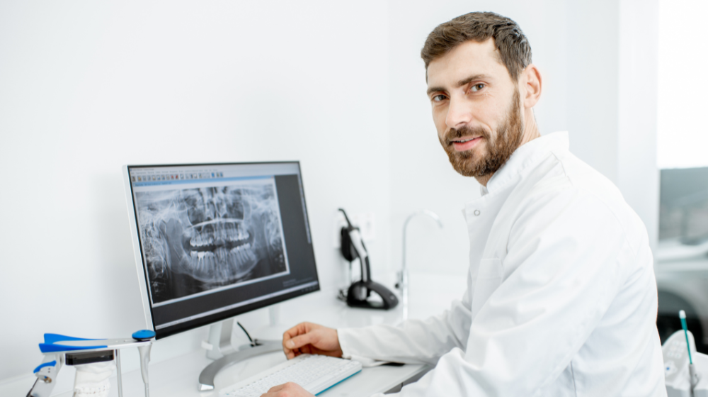 Dentist reviewing a panoramic dental X-ray on a computer monitor in a modern dental office.