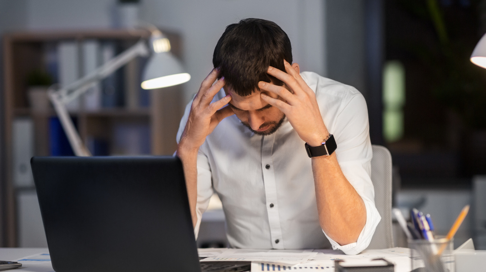 Frustrated dental practice owner reviewing paperwork at a desk late at night, illustrating the hidden operational costs of legacy dental software.