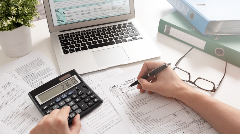Dentist reviewing EBITDA for dental practice with paper, calculator, and laptop